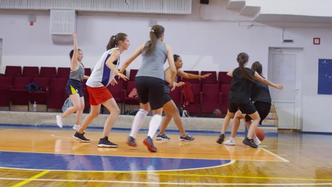 Group of young multiethnic female athletes in sportswear playing basketball while training on indoor court