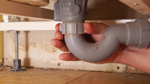 Hand of a plumber man. Locksmith repairs drain under the bath, eliminates clogging. The plumber pulls out a large tuft of hair and debris from the drain.