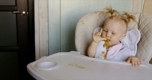 Caucasian baby eating with spoon by itself and getting messy. RAW Graded footage 4K slow motion 60fps 