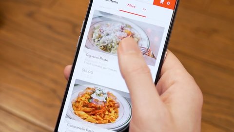 Close-up Ordering takeaway Food Pasta Online in a Restaurant in a Mobile App Using a Smartphone. The Man's Hands Touch The Screen Of His Cell Phone. April 2020, Miami