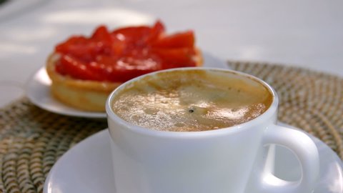 A white sugar cube is falling into espresso coffee in a white cup on the background of french pastry