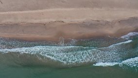 Drone flight over wild beach and turquoise green sea, above waves and sand