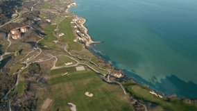 Panoramic video of picturesque landscape with green hills, golf fields and buildings near the rocky coastline of the Black sea, Thracian Cliffs golf and beach resort, Bulgaria.