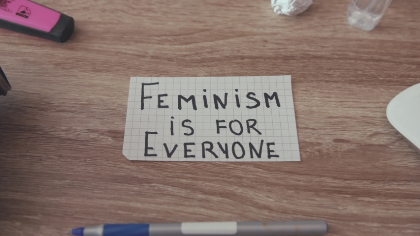 Close up paper on table text Feminism is for Everyone power inside desk woman females feminist girls slow motion