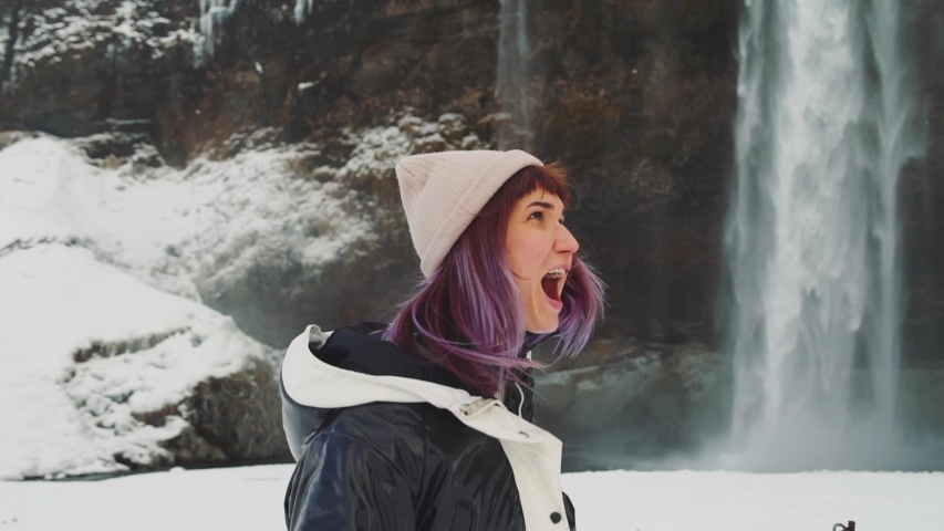 beautiful young woman near a waterfall in Iceland, rejoices and dances