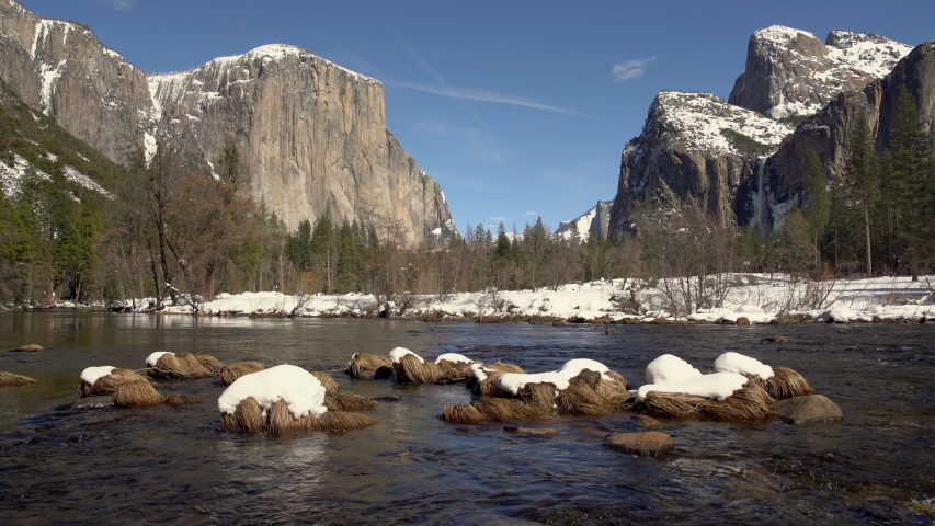 Tracking shot of snow-capped pebbles in Merced River in winter in Yosemite National Park, California 