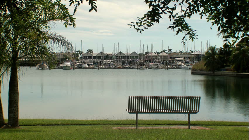 Cullen Bay Marina in Darwin looking toward the moorings with a park bench in the foreground, and with boats,shops and restaurants