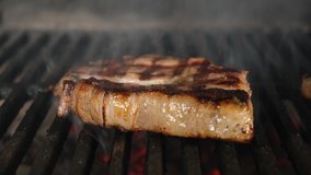 Beef steak meat is cooked over an open fire with heat and smoke of barbecue grill close-up. Dolly sliding video.