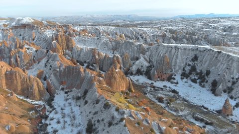 Aerial snowy landscape of Red Valley and Rose Valley at sunset in Cappadocia, Turkey. Aerial cinematic view of Tufa and rock formations covered with snow at Red Valley in Cappadocia.