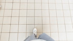 Female legs in sneakers and gray trousers walk on white ceramic tiles in store or hospital. Quarantine, self isolation, depression, social distance, and stay home concept. Stock slow motion video.