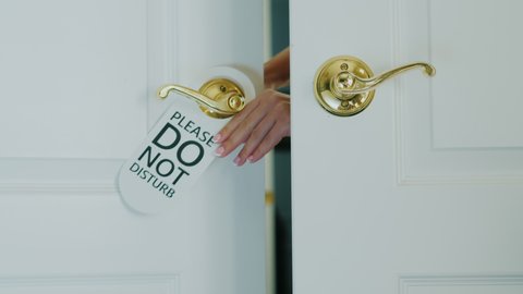 A female hand quickly hangs a Do Not Disturb sign on a door hand.