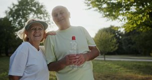 Loving elderly couple posing outdoors in a park backlit by the warm spring sunshine smiling and laughing before turning to each other in a healthy outdoor lifestyle concept
