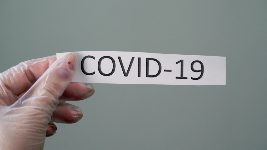 Woman in protective latex gloves holding paper with covid-19 coronavirus text.