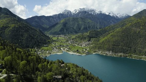 The Improbable aerial landscape of village Molveno, Italy, azure water of lake, empty beach, snow covered mountains Dolomites on background, roof top of chalet, sunny weather, a piers, coastline,