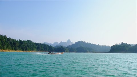 Traditional wooden Thai long-tail boat Sailing with Tourists with mountain background at “Cheow Lan Dam Lake (Ratchaprapha Dam)” Suratthani Thailand.