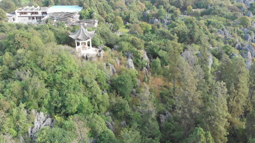 Aerial pan above a Chinese pavilion and an abandoned building in the Stone Forest of Shilin, near Kunming
