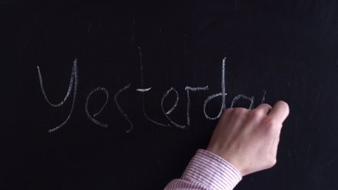 Yesterday with chalk on a blackboard. Top view of the yesterday written in chalk on the board. Yesterday, in a shirt, the hand writes in english.