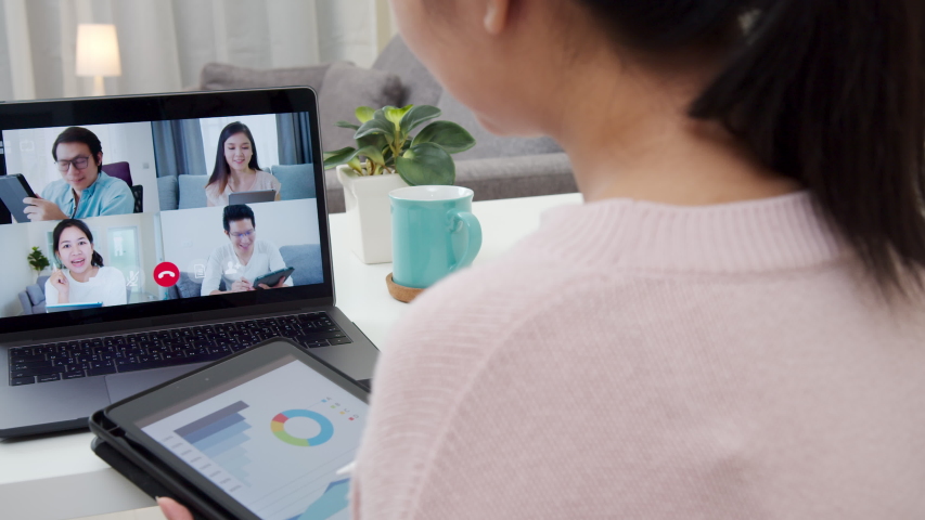 Back view of business woman talking about sale report in video conference.Asian team using laptop and tablet online meeting in video call.Working from home, Working remotely and Self isolation at home Royalty-Free Stock Footage #1051063630