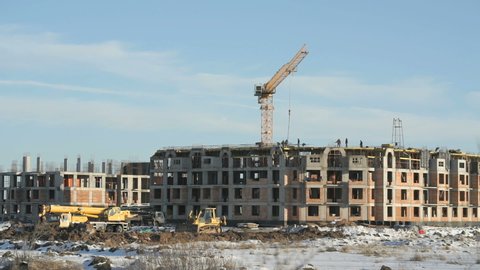 Building large complex in winter. Builders work on the construction site. Construction vehicles outdoors