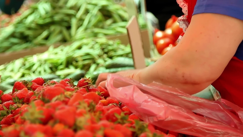 The seller in the market pours strawberries into a bag. | Shutterstock HD Video #1051071634