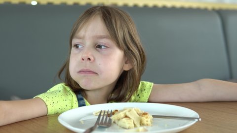 A small child, a girl of European or American appearance, close-up shot. A model eats breakfast at a food court or restaurant. A girl with blond hair 5-6 years old.
