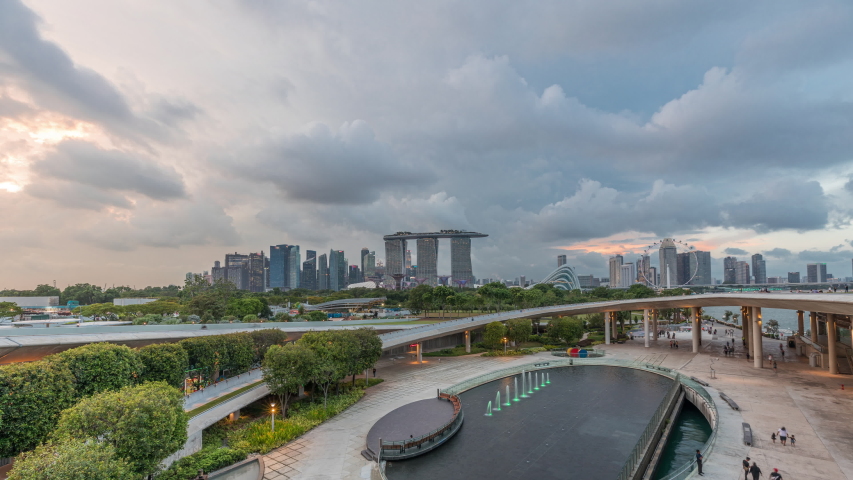 Aerial view after sunset with Singapore city skyline view from Marina barrage garden day to night transition timelapse. Marina barrage has a big fountain in the center and curve walkway lead to the