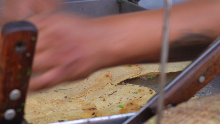 Hispanic indigenous Mexican man making meat pork tacos on street food stall. Hispanic street food seller flipping hot steamy  tortillas by hand on street food stall.