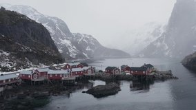 aerial video of famous fishing village called nusfjord located in lofoten islands north of norway. Moody weather, snowing ang cloudy and foggy conditions. Traditional red cabins