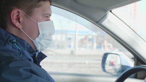 The guy drives the car. Medical mask on the face. People use extra protection against bacteria.