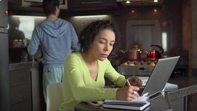Pensive Pretty black female freelancer with curly short hair working online at laptop and taking notes. indoor at kitchen home. language learning, online education, work concept. - Powered by Shutterstock - Get 15% off with code: PIKWIZARD15