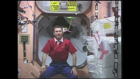 1990s: Astronaut spins double bladed helicopter between hands and releases. Double bladed helicopter spins and floats through space station. Man spins small helicopter toy in hands and releases.