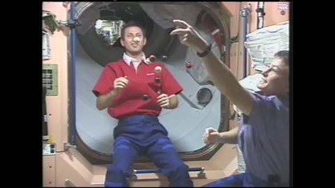 1990s: Astronauts play with floating marbles in zero gravity. Astronauts toss rubber ball into floating wooden balls. Balls float in various directions.