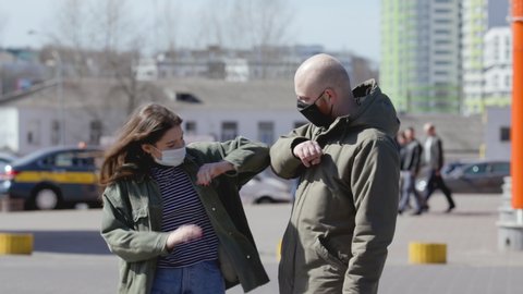 Friends use elbow bump as an alternative greeting to help prevent spread of disease. Young people in medical masks communicate at distance during epidemic.