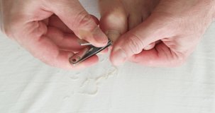 Caucasian young adult male clipping down his own toe nails on the bed white sheets home manicure