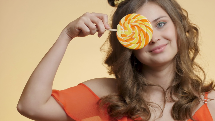 beautiful cute girl with caramel candy on colored studio background, young happy woman have fun with sweet lollipop, concept female bauty and korean style