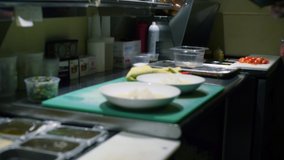 Chef Preparing Dish Inside Restaurant Kitchen. Close up clip as chef adds green beans to the plates with rice and sauce.