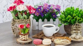 Coffee cup with macaroons and bun with flowers on wooden table background.