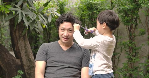 Couple of dad and son at home having fun together, Son with scissors playing at be a barber or hairdresser do haircuts to his father at home. Stay at home quarantine coronavirus pandemic prevention.