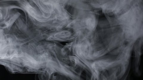 White smoke slowly floats in space on a black background, changing its trajectory. The element of visual effects. An abstract cloud of smoke. Billowing smoke.  