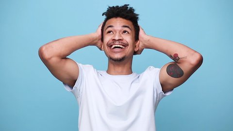 Fun happy african american young guy 20s in white t-shirt posing isolated on blue background studio portrait. People sincere emotions lifestyle concept. Looking at camera found out heard good news