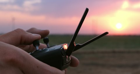 The operator holds a quadcopter control panel in the sunset, closeup.