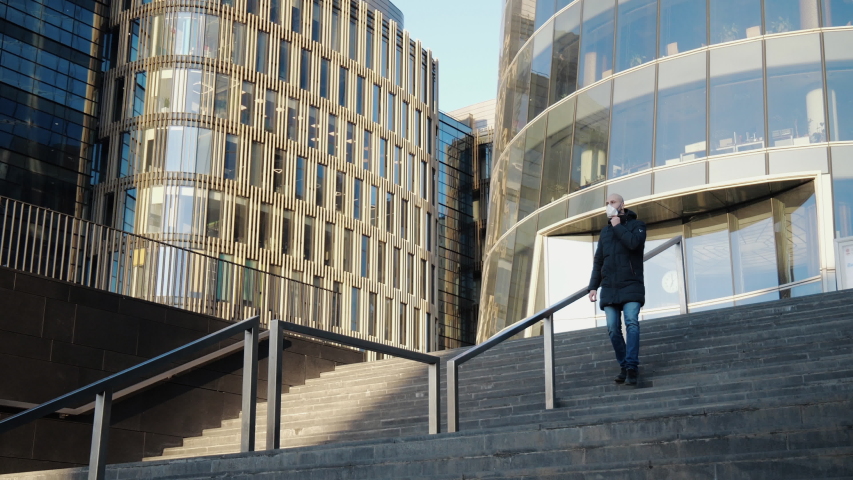 Young guy in a medical mask goes down the stairs against the background of an empty business center