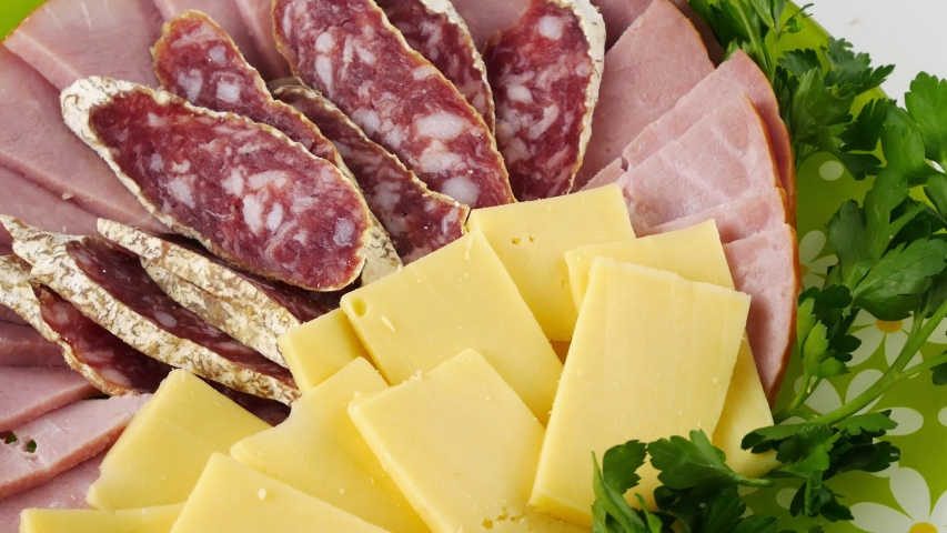 Cold cuts with cheese and herbs,a large portion.Closeup rotating on a green,round plate.Smoked,cured, sausage,pork ham and cream cheese with holes.Delicious,healthy food.