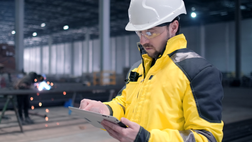 Portrait of Professional Heavy Industry Engineer / Worker Wearing Safety Uniform, Goggles and Hard Hat In the Background Unfocused Large Industrial Factory where Welding Sparks Flying. Safety glasses | Shutterstock HD Video #1051122277