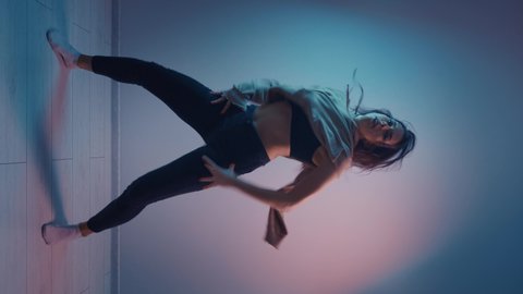 Vertical video of young woman dancer dancing challenge for social network in multi-colours neon lighting room