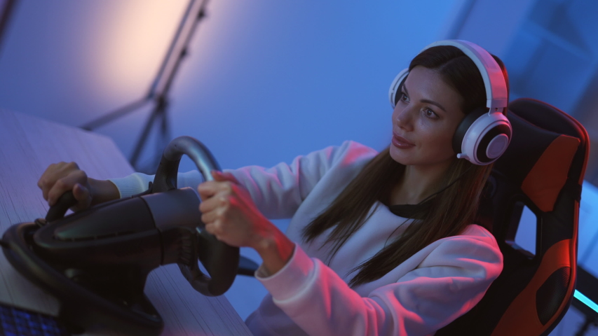 The gamer girl plays video games with steering wheel in the blue light room