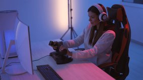 The smiling gamer girl with headphones plays video games in the blue light room