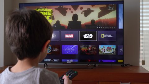 Barcelona, Spain. April 2020: Back view image of cute little boy watching the Star Wars movie and TV series catalog on Disney plus service at the TV screen