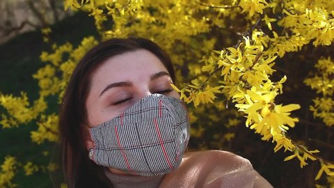 Woman wears reusable handmade mask outdoors during coronavirus covid-19 pandemic. Girl enjoying flowers in garden