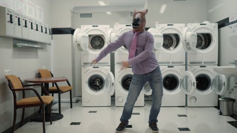 Joyful Man in mask horse Dancing Cheerful In Laundry Room. Man Dancing Viral Dance And Have Fun In Laundry Room. Happy Guy Enjoying Dance, Having Fun Together, Party Halloween. Slow Motion. Halloween